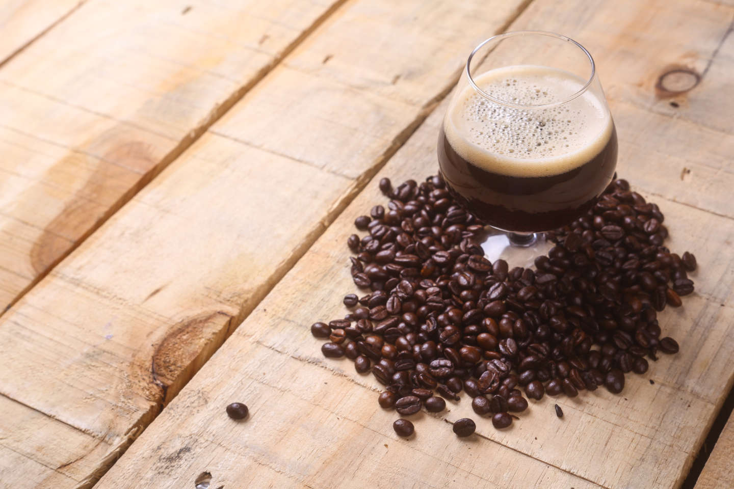 brown beer in glass surrounded by coffee beans