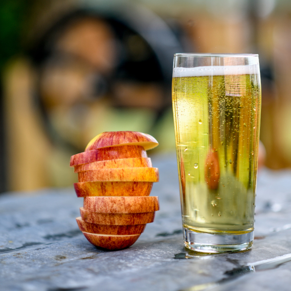 glass of fermented cider next to a sliced apple