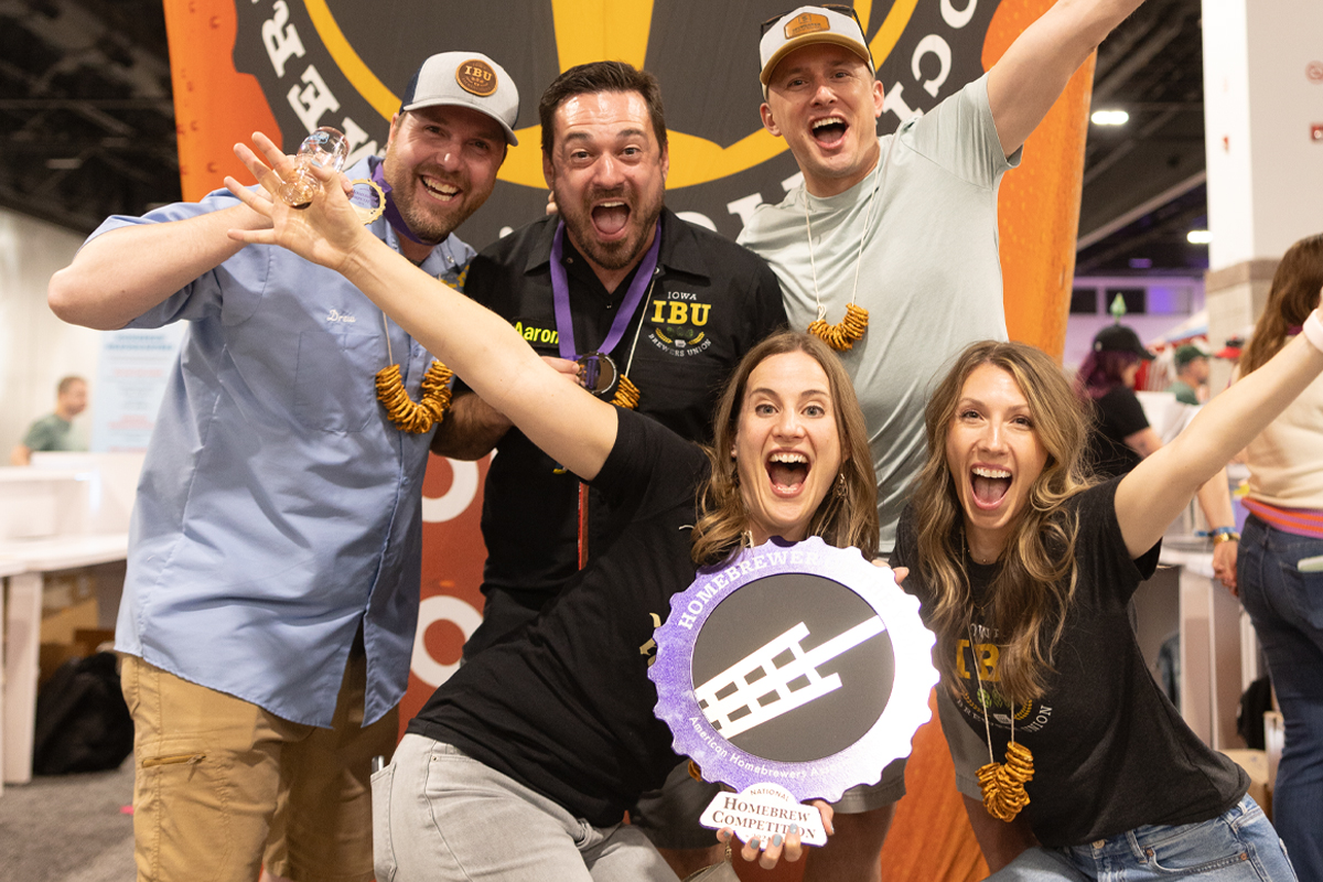A group of people pose in front of a large blow-up beer glass holding an award.